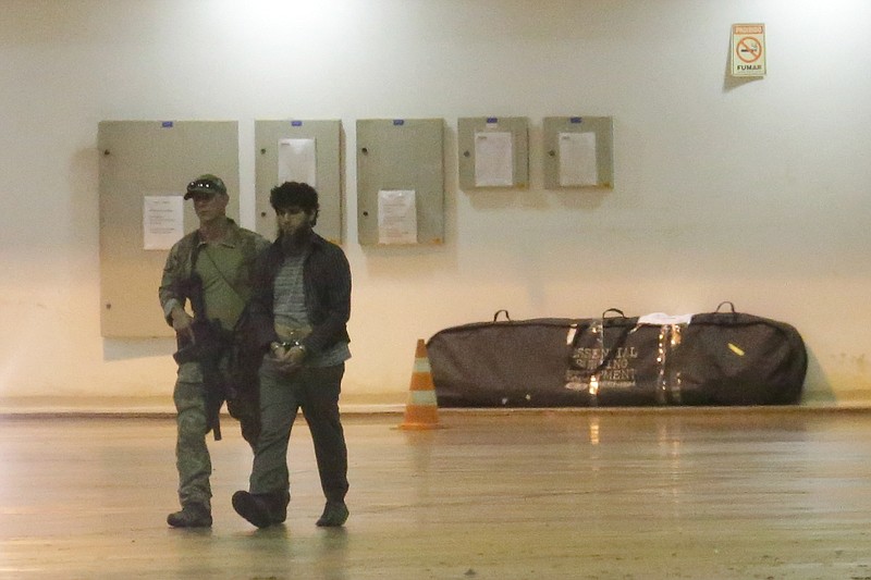A federal police agent leads a handcuffed suspect who authorities say was arrested on terrorism-related charges in Brasilia, Brazil, Thursday, July 21, 2016. Ten Brazilians, who according to authorities pledged allegiance to the Islamic State militant group, were arrested Thursday. Authorities also described them as "amateurs" who discussed on social media the possibility of staging attacks during next month's Olympics. (AP Photo/Eraldo Peres)