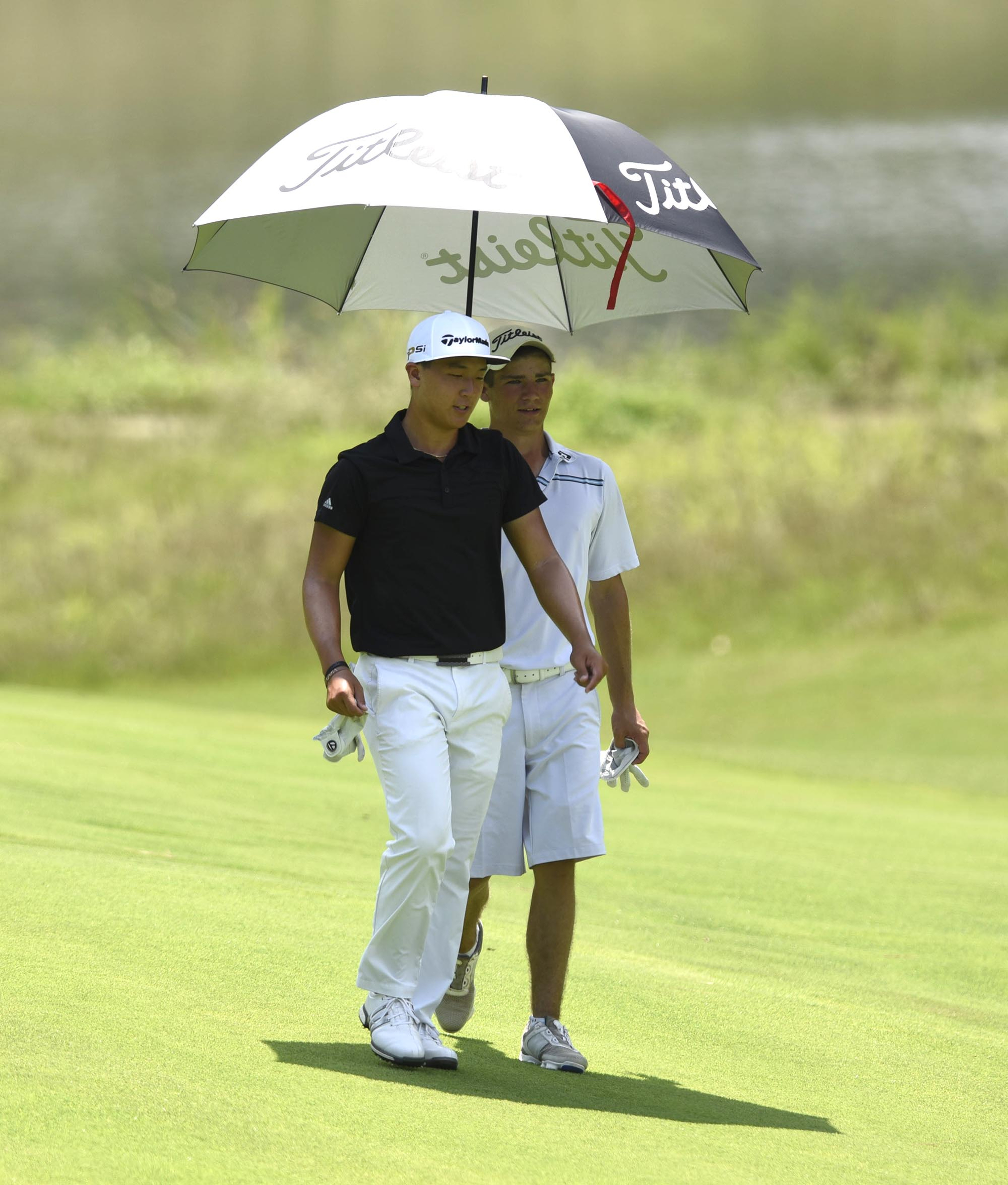 John Pak of Scotch Plains, New Jersey, left, and Noah Goodwin share an umbrella as they walk down the 9th fairway.  Goodwin defeated Pak after 20 holes in the semifinal match.  The fifth day of the 69th U.S. Junior Amateur Championship was held at the Honors Course in Ooltewah, Tennessee, Friday July 22, 2016.