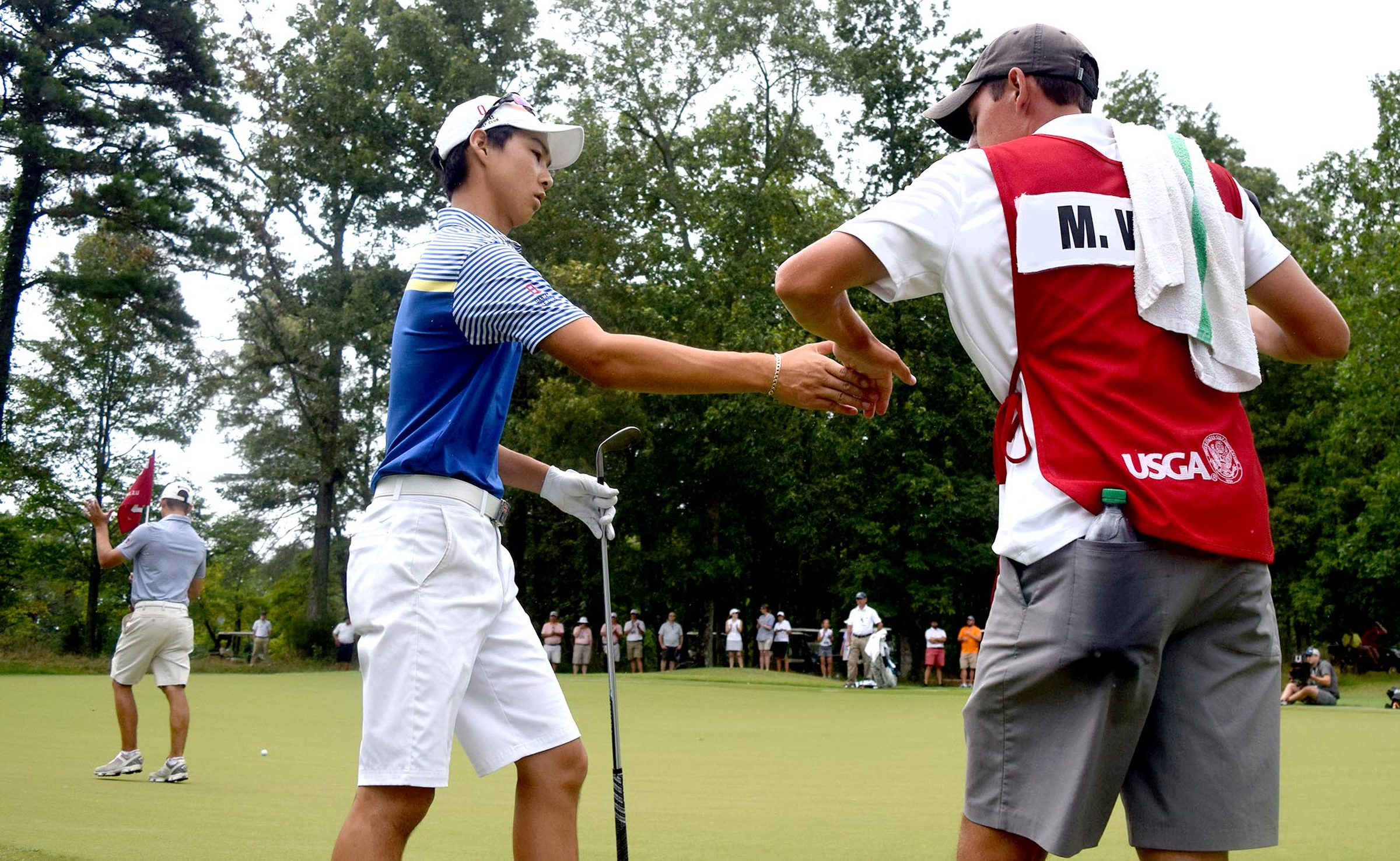 Australia's Min Woo Lee is congratulated by his caddie, Reid Smith, after a chip shot that landed 3 1/2 feet from the 35th hole.  In the background Lee's opponent, Noah Goodwin of Cornith, Texas claps.  The final day of the 69th U.S. Junior Amateur Championship was held at the Honors Course in Ooltewah, Tennessee, Saturday July 23, 2016.