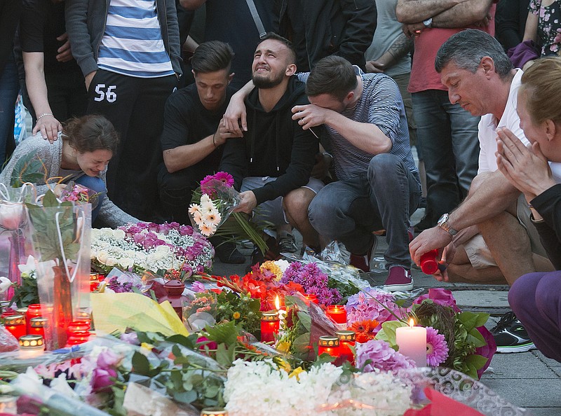 People mourn behind flower tributes near the Olympia shopping center where a shooting took place leaving nine people dead the day before, in Munich, Germany, Saturday, July 23, 2016. Police piecing together a profile of the gunman whose rampage at a Munich mall Friday left nine people dead described him Saturday as a lone, depression-plagued teenager. (AP Photo/Jens Meyer)