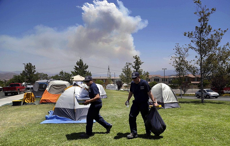 
              In this Tuesday, July 26, 2016 photo, firefighters carry food and supplies past dozens of firefighter tents covering a field at a firefighter operations base camp that has been established at Golden Valley High School in Santa Clarita, Calif., as smoke from the Sand fire looms up in the background. When a wildfire becomes too big for local departments to handle alone, an incident command network is activated to to coordinate the large numbers of people, equipment and supplies needed for these operational bases. (AP Photo/Nick Ut)
            