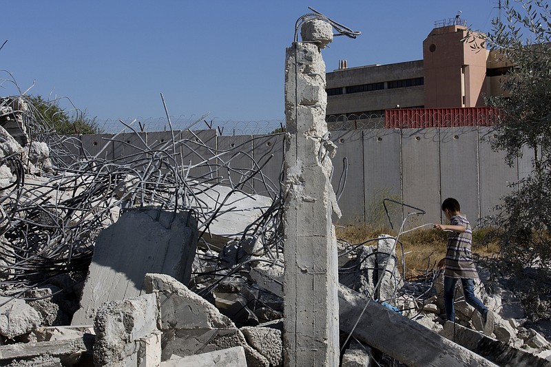 
              A Palestinian boy walks over the rubble of a house that overlooks the Israeli separation barrier, background, and was demolished by the Israeli army, in the West Bank village of Qalandia, near Ramallah, Tuesday, July 26, 2016. Israeli army bulldozers demolished elven houses along side the Israeli separation barrier, at the village of Qalandia early morning. The Israeli B'Tselem rights group reported last Monday that Israeli authorities demolished 168 homes in the West Bank from January to the end of June this year. (AP Photo/Nasser Nasser)
            