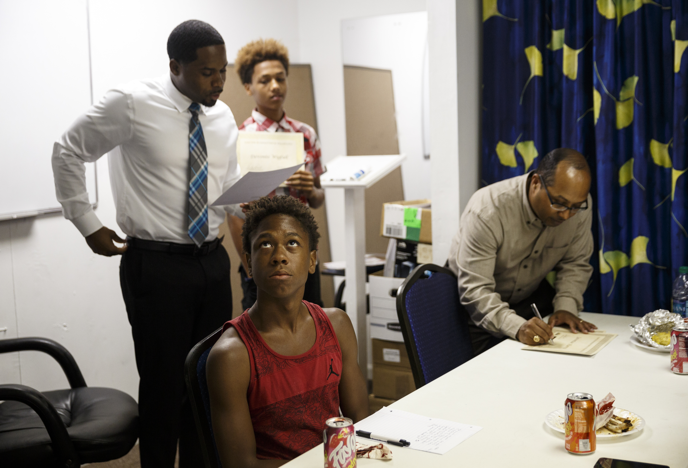 Malik Henry looks up as his name is called by Marcellus Barnes, left, to receive a certificate signed by Oliver Richmond, right, at a celebration luncheon at Front Porch Alliance on Friday, July 29, 2016, in Chattanooga, Tenn. Henry was among among 5 students who were paid $10 an hour over the summer to learn money management and lawn work.