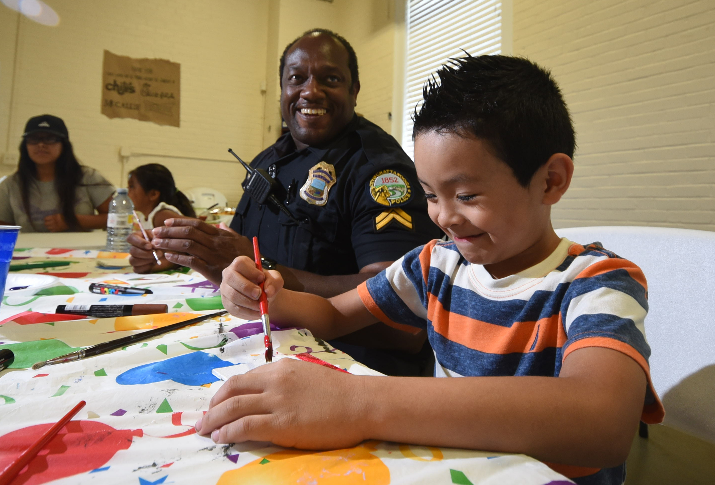 Julian Grimaldo, right, gets a smile from Chattanooga Police Officer Ernest Craw as they work to paint their piece of art for the Unity Mosaic Project on Tuesday at the Ridgedale Outreach Center.