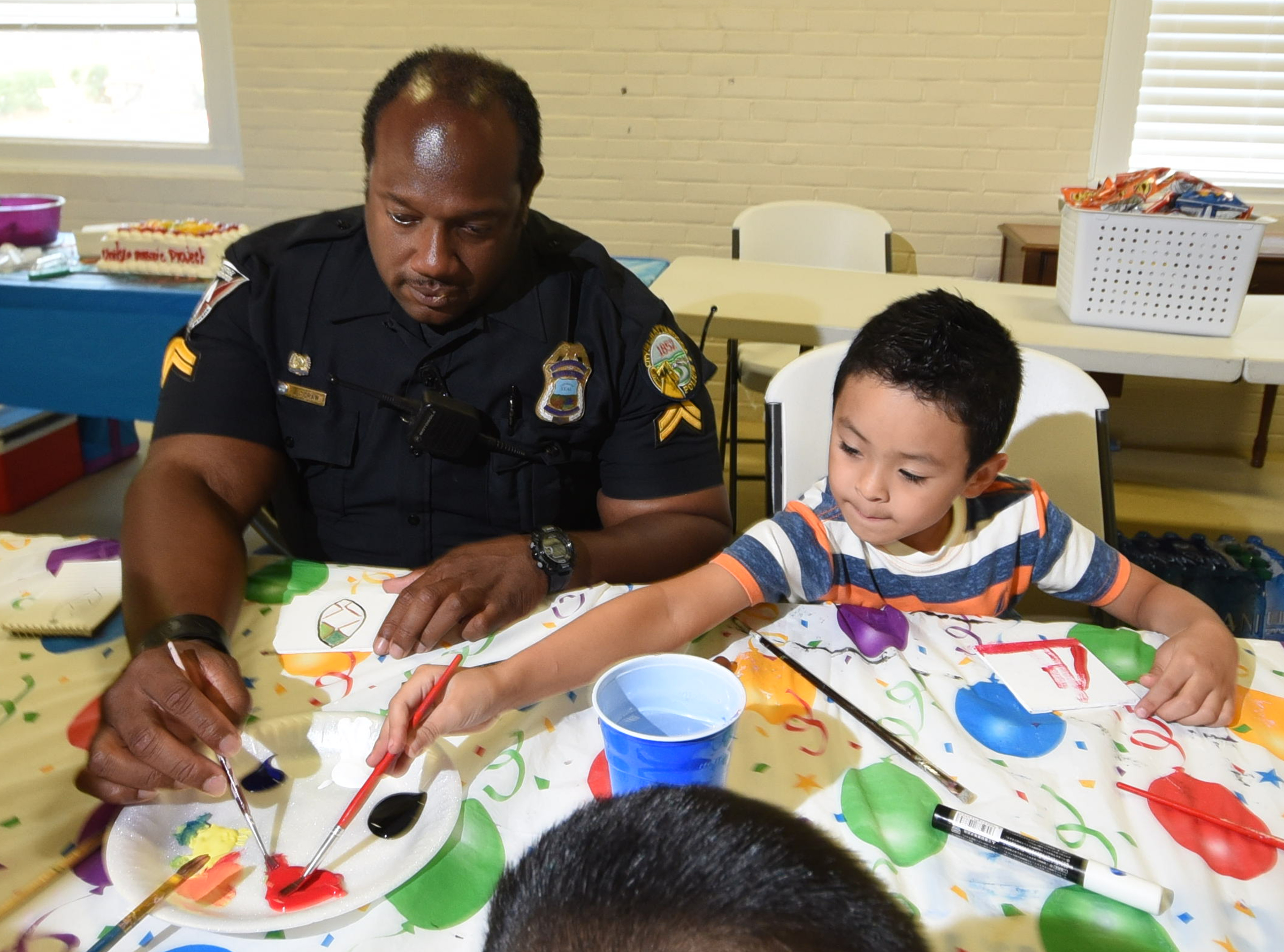 Julian Grimaldo, right, reaches for more paint with  Chattanooga Police Officer Ernest Craw as they work to paint their piece of art for the Unity Mosaic Project on Tuesday at the Ridgedale Outreach Center.
