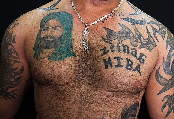 In this Tuesday, July 19, 2016 photo, Zulfiqar, 30, poses for a photo showing his tattoo of Shiite Muslims' first Imam Ali, left, in the southern suburb of Beirut, Lebanon. A growing number of Shiite Muslims in Lebanon are getting tattoos with religious and other Shiite symbols since the civil war in neighboring Syria broke out five years ago, fanning sectarian flames across the region. (AP Photo/Hassan Ammar)