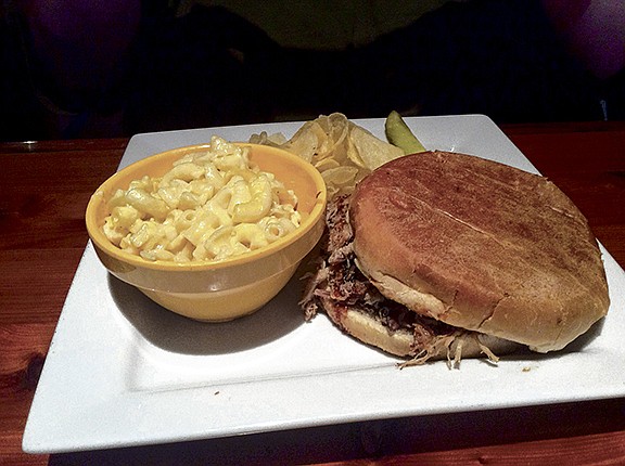 A large pulled-pork sandwich and side of mac-and-cheese, chips and a pickle are displayed at Sportsman's BBQ.