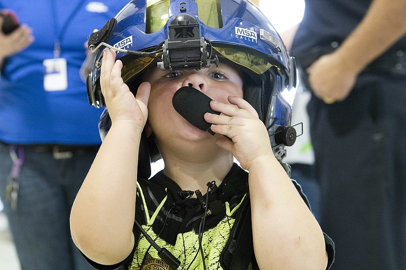 In this Wednesday, August 10, 2016, photo, 3-year-old Joshua Collins tries on a flight helmet while touring Knox County Sheriff's Office's aviation unit in Knoxville, Tenn. The youngster from Rocky Top, Tenn., is a big fan of Batman and thinks every law enforcement officer is the super hero, so his mother has taken him to visit several police departments. But Wednesday's stop was special because he was getting to see a "bat copter." (Saul Young/Knoxville News Sentinel via AP)
