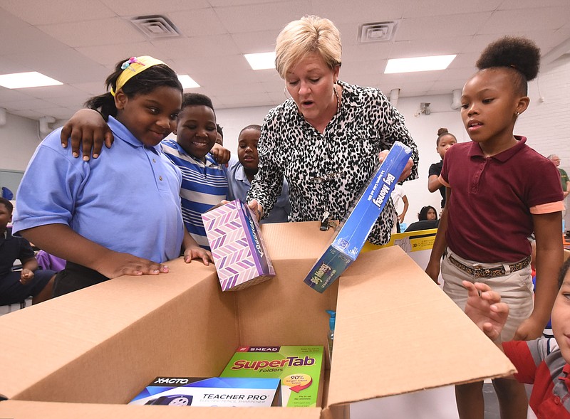 Woodmore 4th grade math and science teacher Cherri Sehrick, center, looks through the gift box from Amazon with her students on Tuesday morning during an assembly in the cafetorium. From left are, Syler Pollard, Odareyon Cox, Sehrick and R'Shyana Timmons. 