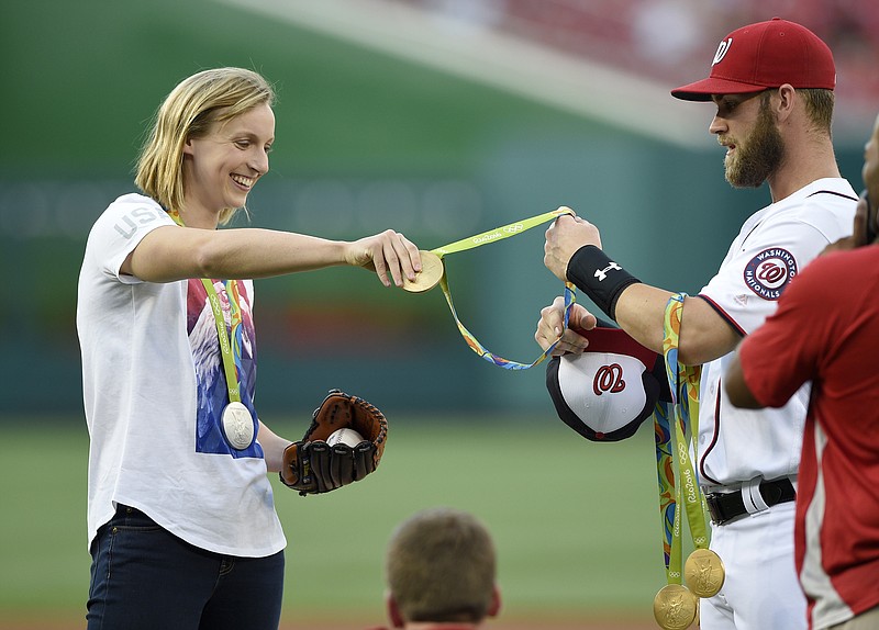 
              Olympic gold medal swimmer Katie Ledecky, left, hands her medals to Washington Nationals' Bryce Harper, right, to hold before she threw out the ceremonial first pitch before a baseball game between the Baltimore Orioles and the Washington Nationals, Wednesday, Aug. 24, 2016, in Washington. (AP Photo/Nick Wass)
            