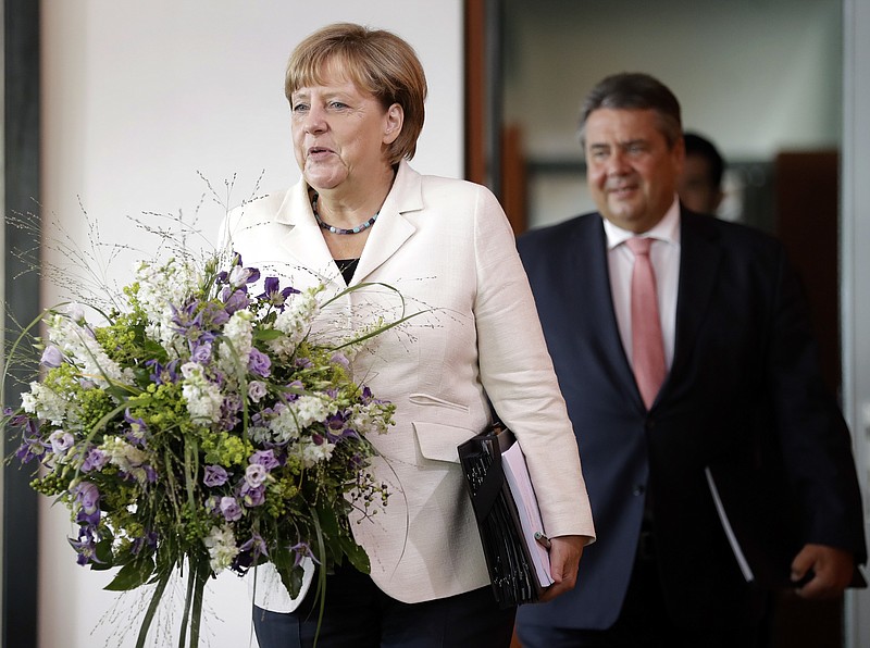 
              German Chancellor Angela Merkel, left, holds a bunch of flowers as a birthday present for a member of the cabinet during her arrival for the weekly cabinet meeting at the Chancellery in Berlin, Germany, Wednesday, Aug. 24, 2016. At right is German Minister for Economic Affairs and Energy Sigmar Gabriel. (AP Photo/Michael Sohn)
            