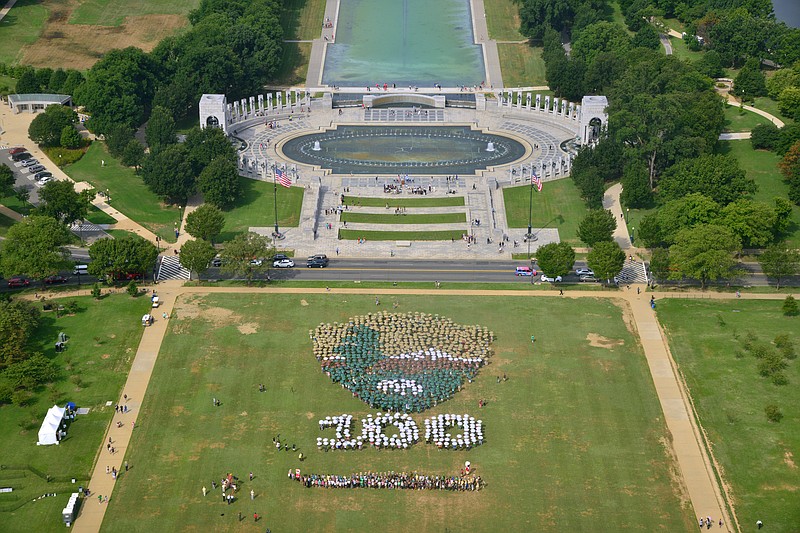 
              This photo provided by the National Park Service shows people on the National Mall in Washington, looking toward the World War II Memorial, Thursday, Aug. 25, 2016, creating a giant, living version of the National Park Service emblem. Participants used brown, green and white umbrellas to create the emblem. 
(Tim Ervin/National Park Service via AP)
            