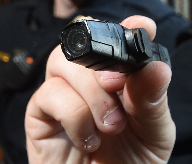 Chattanooga Police Officer Jeff Buckner holds an AXON FLEX personal body camera that measures approximately 4-inches long. Buckner's camera mounts to a pair of sunglasses he is wears.