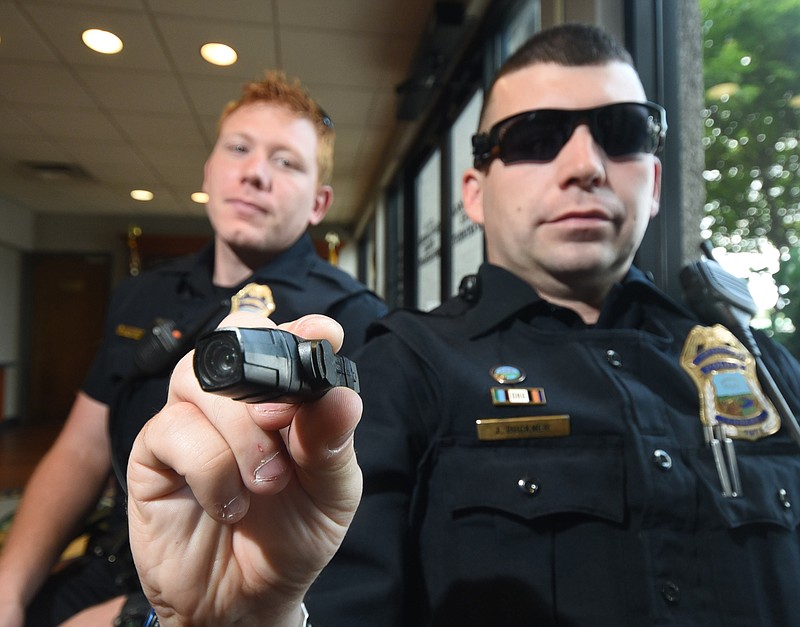 Chattanooga Police Officer Jeff Buckner holds is AXON FLEX personal body camera that he is testing for the department on Thursday in the lobby of the Police Service Center on Amnicola. Buckner's camera mounts to the pair of sunglasses he is wearing. Officer Hunter Morgan, left, is testing a chest mounted body cam.