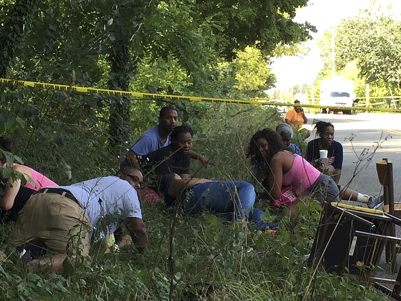 Bystanders take cover in a ditch as a fight breaks out at the scene of a triple shooting.