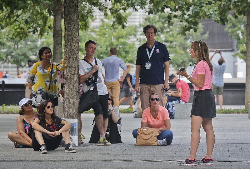 Jean Nebbia, far right, a schoolteacher from Oakland, N.J., talks with visitors to the Sept. 11 memorial site, Thursday Aug. 11, 2016, in New York. Nebbia serves as a volunteer tour guide, organized by the private nonprofit 9/11 Tribute Center, to tell tours about her brother Steven Schlag, a partner at Cantor Fitzgerald, who was killed in the Sept. 11 attacks on the World Trade Center. (AP Photo/Bebeto Matthews)