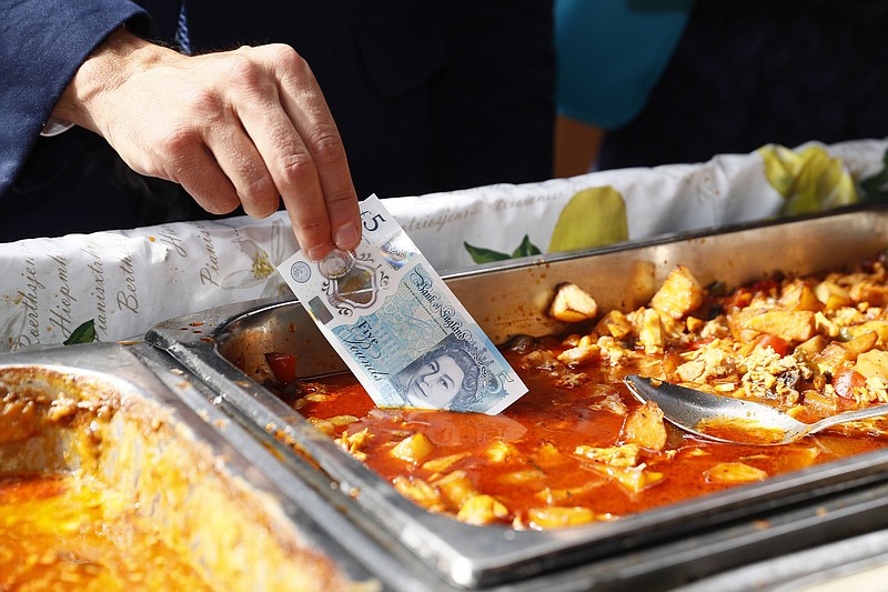 
              Bank of England Governor Mark Carney dips a new plastic £5 note into a tray of food as he buys lunch from a stall at Whitecross Street market in London, Tuesday, Sept. 13, 2016. The polymer fiver is said by the Bank of England to be cleaner, safer and stronger than paper notes, lasting around five years longer. (Stefan Wermuth/Pool Photo via AP)
            