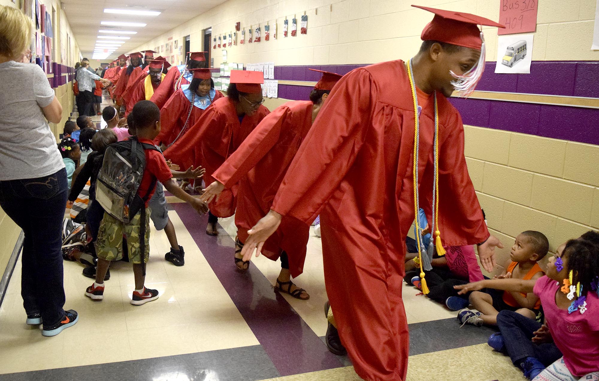 Brainerd Seniors bent to high five some of the younger Orchard Knob Elementary students. The 2016 graduating class of Brainerd High School walked through the halls of Orchard Knob Elementary in their caps and gowns, as a representation of the "vision" for where the elementary students will one day be.