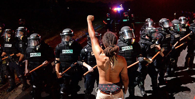 A protester stands with his left arm extended and fist clenched in front of a line of police officers in Charlotte, N.C. on Tuesday, Sept. 20, 2016. Authorities used tear gas to disperse protesters in an overnight demonstration that broke out Tuesday after Keith Lamont Scott was fatally shot by an officer at an apartment complex. (Jeff Siner/The Charlotte Observer via AP)