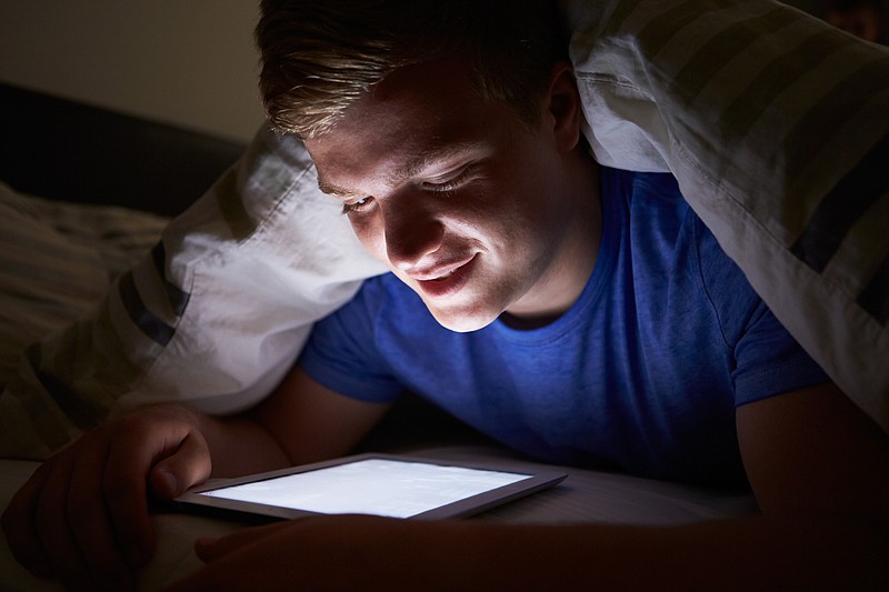 Teenage Boy Using Digital Tablet In Bed At Night Under Covers