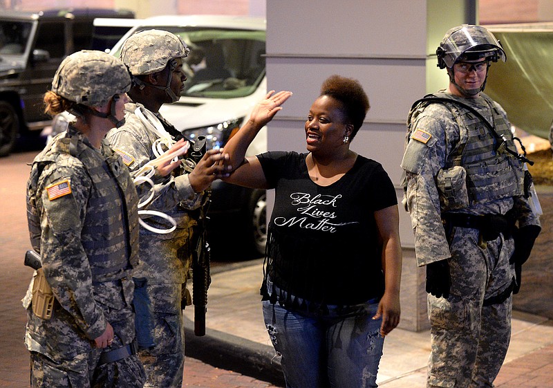 An activist slaps high fives with members of the National Guard in Charlotte, N.C. Friday, Sept. 23, 2016. Protesters marched through the streets of Charlotte on Friday to protest Tuesday's fatal police shooting of Keith Lamont Scott. After darkness fell, dozens or people carried signs and chanted to urge police to release dashboard and body camera video that could show more clearly what happened. (Jeff Siner/The Charlotte Observer via AP)