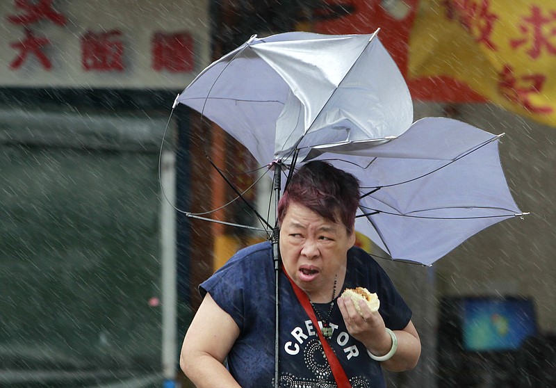 
              A woman eats and struggles with her umbrella against powerful gusts of wind generated by typhoon Megi across the the island in Taipei, Taiwan, Tuesday, Sept. 27, 2016. Schools and offices have been closed on Taiwan and people in dangerous areas have been evacuated as a large typhoon with 162 kilometers- (100 miles-) per-hour winds approaches the island. (AP Photo/Chiang Ying-ying)
            