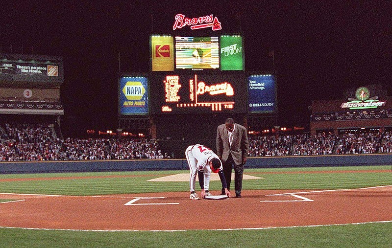 In this April 4, 1997, file photo, former Atlanta Braves great Hank Aaron looks on as pitcher Tom Glavine places down home plate from Atlanta Fulton County Stadium on top of the plate at Turner Field before the Braves opened their new home against the Chicago Cub in Atlanta. Turner Field began its brief life as the main stadium for the 1996 Summer Olympics. After just two decades as the home of the Atlanta Braves, it's headed for another transformation. The Braves are moving to the suburbs next season, leaving the Ted to Georgia State University. (AP Photo/John Bazemore, File)