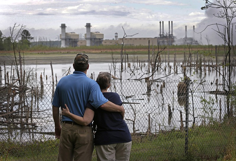 
              FILE - In this April 25, 2014, file photo, Bryant Gobble, left, embraces his wife, Sherry Gobble, right, as they look from their yard across an ash pond full of dead trees toward Duke Energy's Buck Steam Station in Dukeville, N.C. Duke Energy has agreed to remove millions of tons of coal ash containing toxic heavy metals from a power plant in North Carolina. The nation’s largest electricity company announced Wednesday, Oct. 5, 2016  that it would dig up three huge pits of water-logged ash at the Buck Steam Station near Salisbury. The ash will be dried and either offered for use in making concrete or moved to lined landfills elsewhere.  (AP Photo/Chuck Burton, File)
            