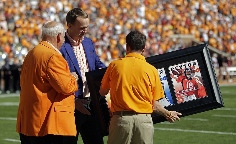 Former Denver Broncos and Tennessee quarterback, Peyton Manning is presented framed Sports Illustrated covers by former head football coach Phillip Fulmer, left, and athletic director Dave Hart before an NCAA college football game against Alabama Saturday, Oct. 15, 2016, in Knoxville, Tenn. (AP Photo/Wade Payne)