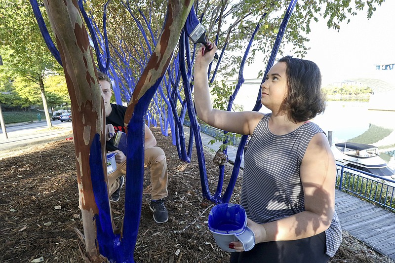 Staff Photo by Dan Henry / The Chattanooga Times Free Press- 10/18/16. The University of Tennessee at Chattanooga sophomores Caleb Mathias and Rachel Frizzell paint trees blue with artist Konstantin "Kon" Dimopoulos under the Market Street Bridge along Riverfront Parkway on Tuesday, October 18, 2016. 