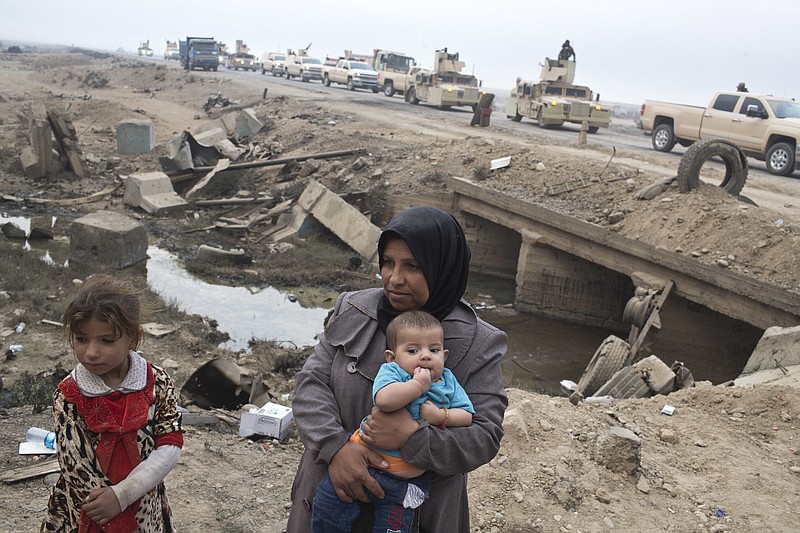 Internally displaced persons stand at a checkpoint as an Iraqi army convoy passes by in Qayyarah, about 31 miles (50 km) south of Mosul, Iraq, Sunday, Oct. 23, 2016. The U.N. and aid organizations say that some 5,000 civilians have been displaced since the operation to retake the city of Mosul from Islamic State began, a tiny fraction of the estimated one million remaining inside the city. (AP Photo/Marko Drobnjakovic)