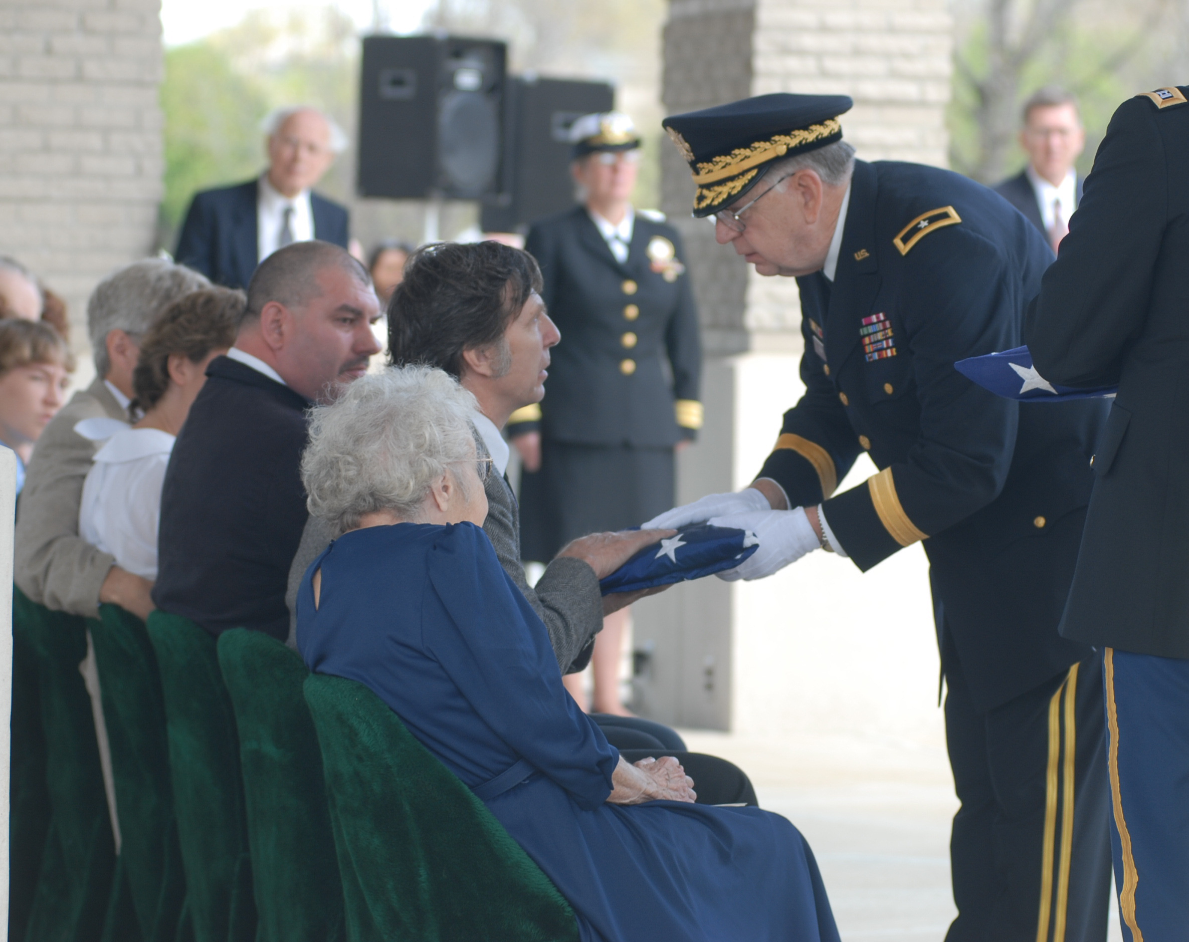 Brigadier General Carl E. Levi, (Ret.) presents Desmond Doss, Jr., a folded flag from the casket of his father, Medal of Honor recipient Desmond Doss, at the conclusion of graveside services at the Chattanooga National Cemetery in 2006. Seated on the end of the row is Frances Doss, widow of Desmond Doss.