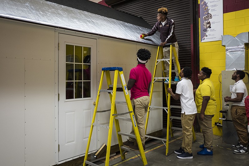 Students watch as Kemarkus Young stands on a ladder to flatten out reflective roofing on a Tiny House under construction at Tyner Academy on Wednesday, Oct. 26, 2016, in Chattanooga, Tenn. Students in Jerry Webb's class have been constructing the environmentally friendly Tiny House, which will include a solar power system, to learn about renewable energy and sustainability.