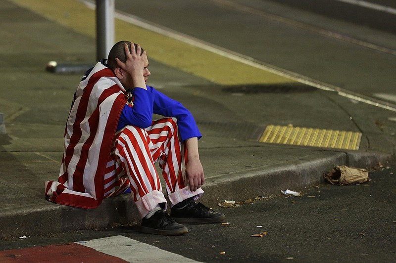 A man dressed in red-white-and-blue sits on the curb during a protest against President-elect Donald Trump, Wednesday, Nov. 9, 2016, in Seattle's Capitol Hill neighborhood. (AP Photo/Ted S. Warren)