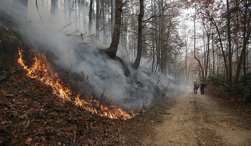 Firefighters walk down a dirt road a wildfire burns a hillside Tuesday, Nov. 15, 2016, in Clayton, Ga. On Tuesday, the Tennessee Valley Authority issued a burn ban on its public lands across Tennessee and in parts of Alabama, Georgia, Kentucky, Mississippi, North Carolina and Virginia. U.S. Forest Service spokesman Adam Rondeau has said the agency is tracking wildfires that have burned a total of 80,000 acres across the South.