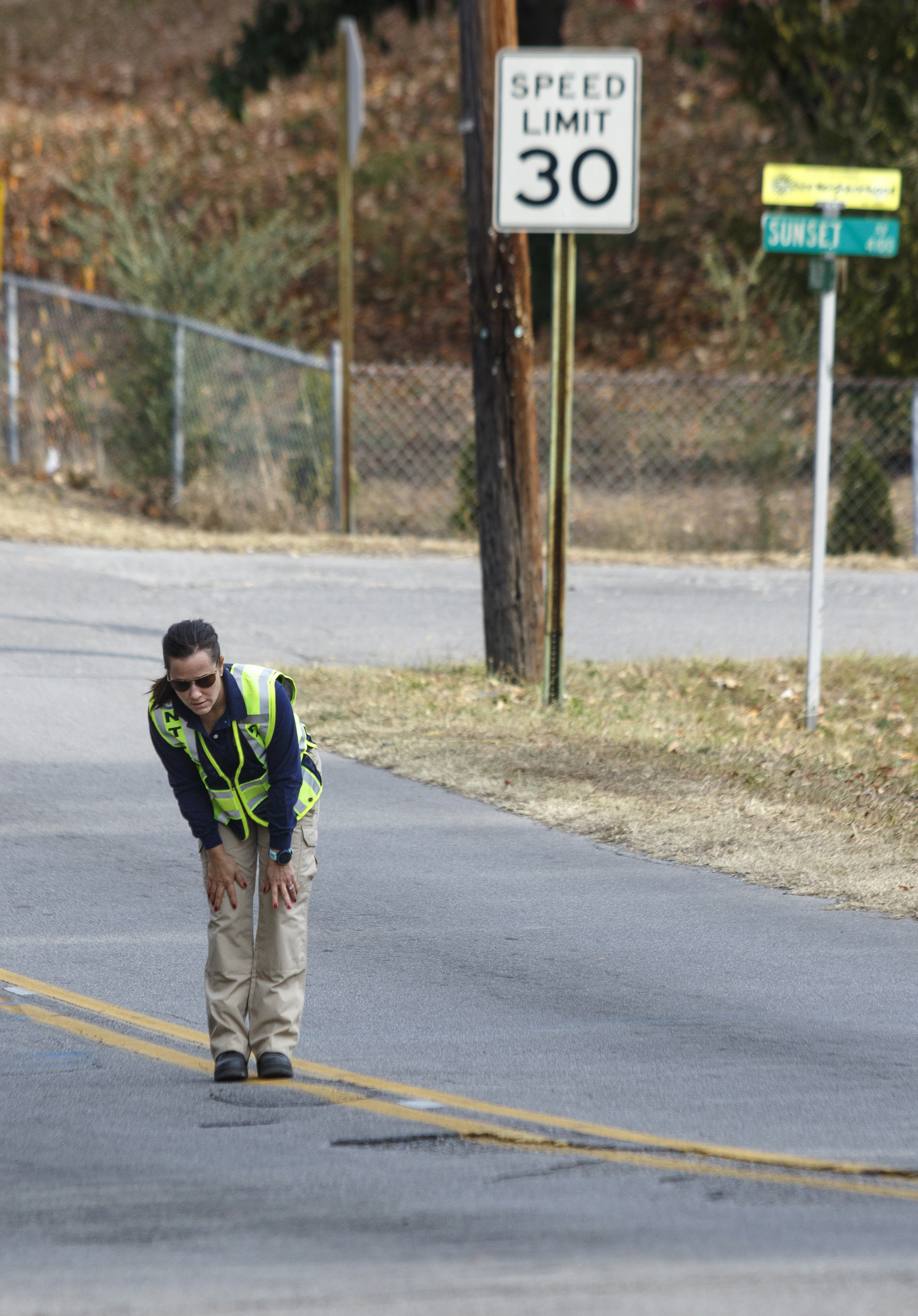 NTSB investigator Michele Beckjord examines the road at the site of a fatal school bus crash on Talley Road on Wednesday, Nov. 23, 2016, in Chattanooga, Tenn. A makeshift memorial to victims of the Monday crash, which killed 5 Woodmore Elementary students and injured dozens more, has grown since the road was reopened Tuesday.