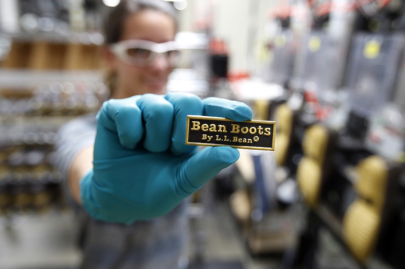 
              FILE - In this Dec. 2, 2014, file photo, Talitha Donaldson displays a label that will be glued onto the back of an L.L. Bean boot, at a facility in Lewiston, Maine. The Maine-based outdoors retailer is installing a third injection-molding machine to manufacture the rubber soles, boosting capacity and creating jobs in Lewiston. (AP Photo/Robert F. Bukaty, File)
            