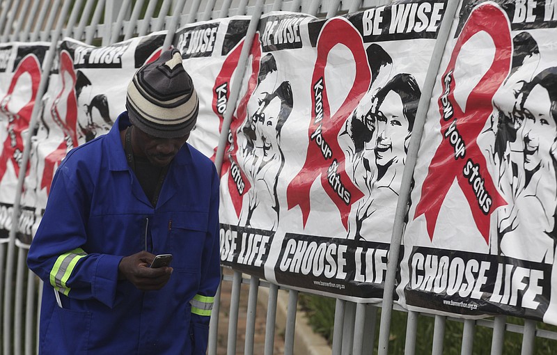 
              FILE -- In this Dec. 1, 2014 file photo a man makes a call on a mobile phone as he passes World AIDS Day banners on the perimeter of an office building in Sandton, Johannesburg, South Africa.  A new vaccine against HIV, called HVTN 702, is to be tested in South Africa, it is announced Sunday Nov. 27, 2016, and scientists aims to enroll 5,400 sexually active men and women for the clinical trial. (AP Photo/Denis Farrell, File)
            