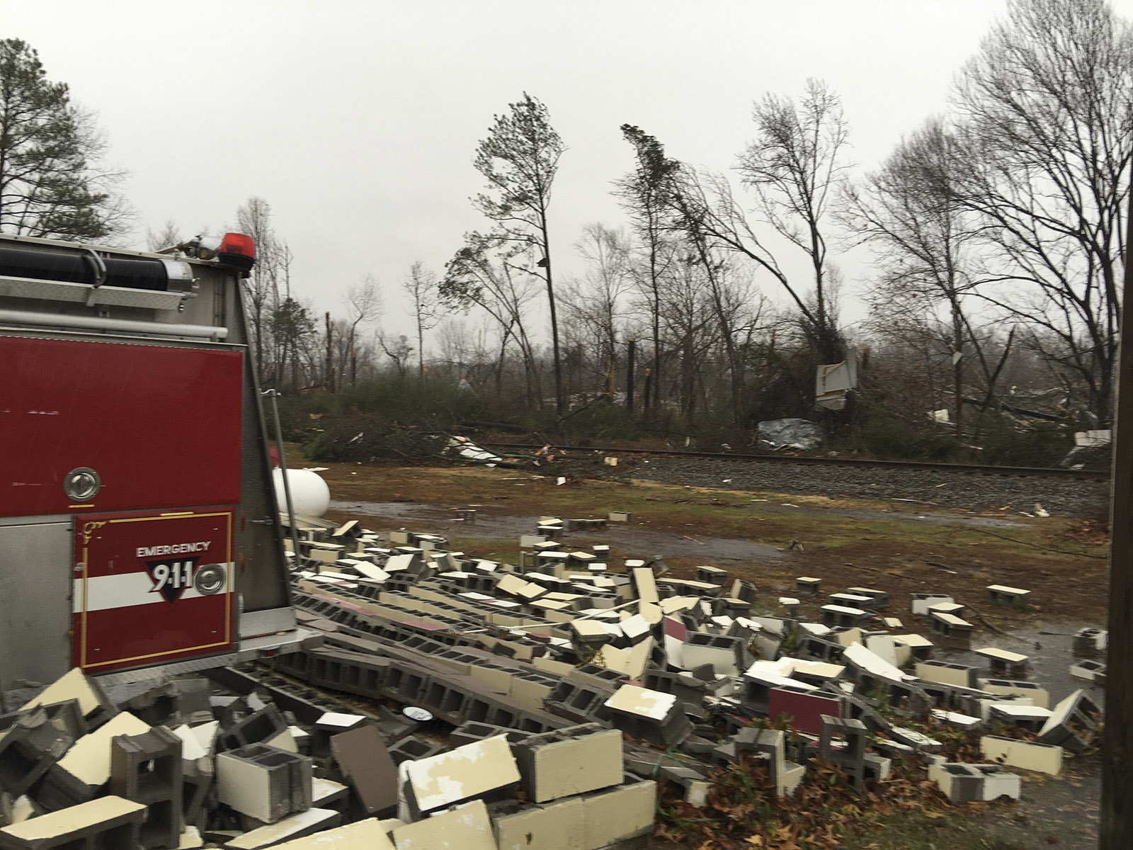 The storm left a wake of damaged and destroyed structures, visible through a screen of trees and across the CSX railroad track in the vicinity of the West Polk Volunteer Fire Hall. Public safety officers have blocked access to the structures on a nearby road.