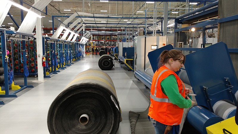 Above: A Shaw Industries employee drops a roll of fabric during the carpet tile production process at the company's new factory. Below: Shaw Industries employees check out carpet tile production equipment at the factory.