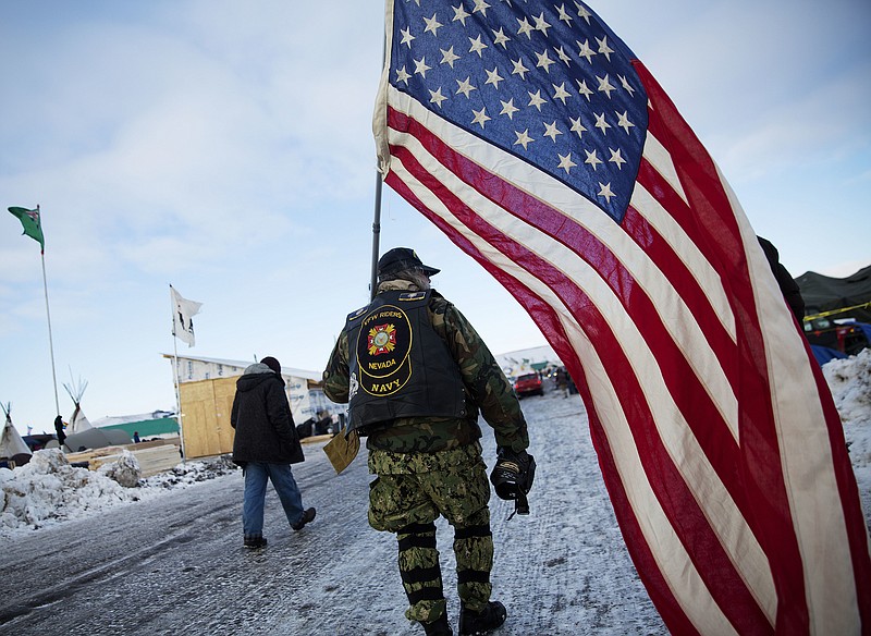 Navy veteran Rob McHaney, of Reno, Nevada, walks with an American flag at the Oceti Sakowin camp where people have gathered to protest the Dakota Access oil pipeline in Cannon Ball, N.D., Sunday. (AP Photo/David Goldman)