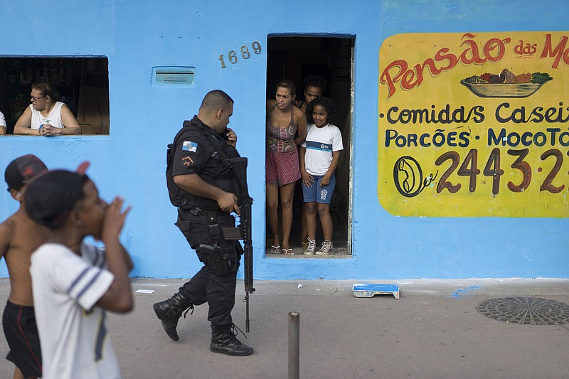 
              In this Nov. 24, 2016 photo, a police officer walks past residents watching a protest against police violence in the City of God slum, in Rio de Janeiro, Brazil. Residents say they are being targeted by police because of the Nov. 19 crash near the slum of a military helicopter on an anti-drug operation, killing the four officers on board. (AP Photo/Leo Correa)
            