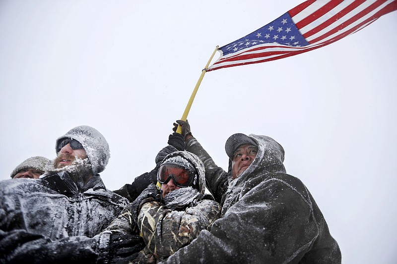 
              Military veterans huddle together to hold a United States flag against strong winds during a march to a closed bridge outside the Oceti Sakowin camp where people have gathered to protest the Dakota Access oil pipeline in Cannon Ball, N.D., Monday, Dec. 5, 2016. (AP Photo/David Goldman)
            