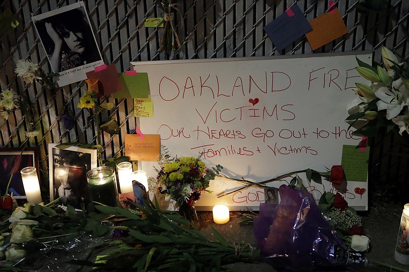 Candles, photos and flowers are placed at a makeshift memorial near the site of a warehouse fire Monday, Dec. 5, 2016, in Oakland, Calif. The death toll in the fire climbed Monday with more bodies still feared buried in the blackened ruins, and families anxiously awaited word of their missing loved ones.