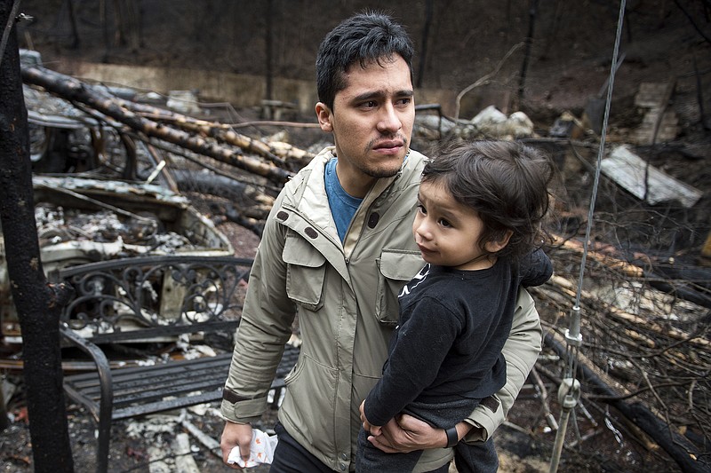 Allan Rivera holds onto his son Nathan Rivera, 23 months old, as he looks at the remains of their home for the first time Monday, Dec. 5, 2016, in Gatlinburg, Tenn. The family evacuated from their rental cabin before it was completely destroyed by a wildfire. A week ago on Monday, hurricane-force winds whipped up fires that killed over a dozen people and damaged or destroyed over a 1,000 buildings in the Great Smoky Mountains tourist region. (Andrew Nelles/The Tennessean via AP)
