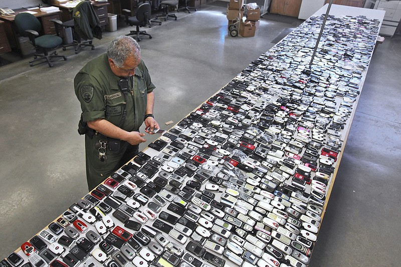 
              FILE - In this April 10, 2009, file photo, Correctional Officer Jose Sandoval inspects one of the more than 2,000 cell phones confiscated from inmates at California State Prison, Solano in Vacaville, Calif. California is installing nearly 1,000 sophisticated metal detectors and scanners at its prisons in its latest attempt to thwart the smuggling of cellphones. (AP Photo/Rich Pedroncelli, File)
            