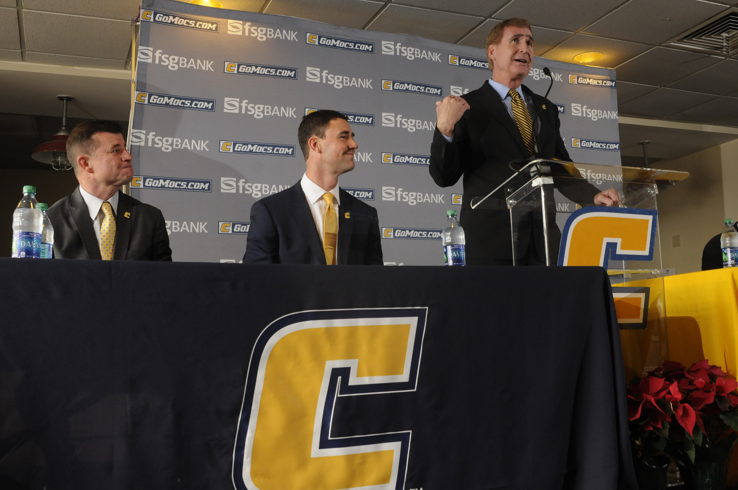 Tom Arth, center, listens as University of Tennessee at Chattanooga Chancellor Steve Angle introduces the new coach to Chattanooga for the first time at the Stadium Club on Tuesday. Athletic Director David Blackburn listens, left.