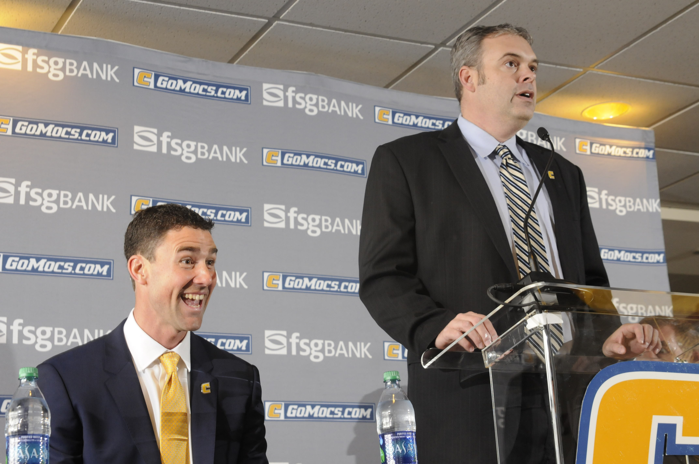 UTC Head Football Coach Tom Arth, seated, reacts to one of his children as Jay Blackman, senior associate athletic director, begins to introduce the new leader of the Chattanooga Mocs football team Tuesday inside the Stadium Club at Finley Stadium.