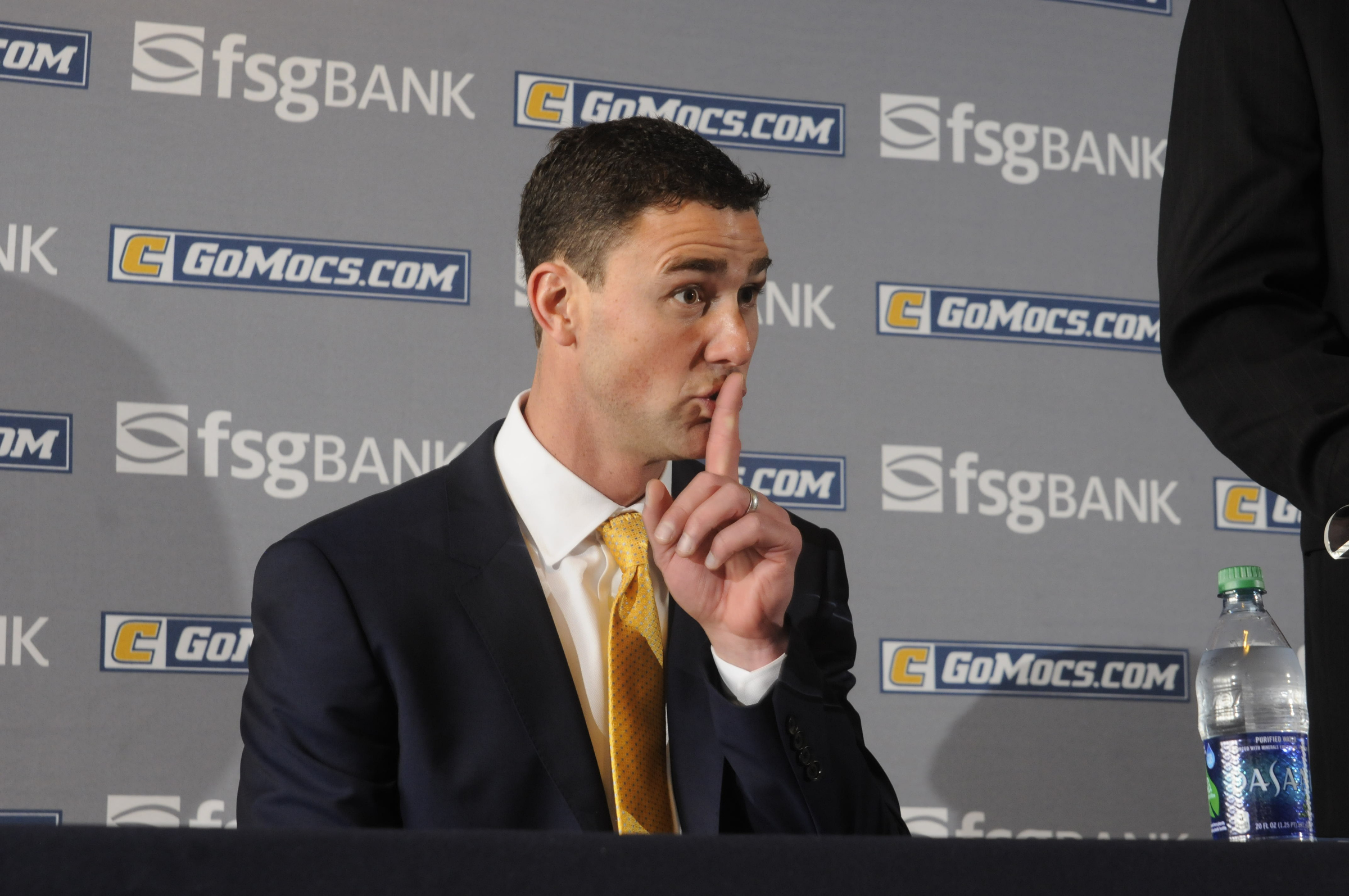 UTC Head Football Coach Tom Arth, seated, reacts to one of his children as Jay Blackman, senior associate athletic director, begins to introduce the new leader of the Chattanooga Mocs football team Tuesday inside the Stadium Club at Finley Stadium.