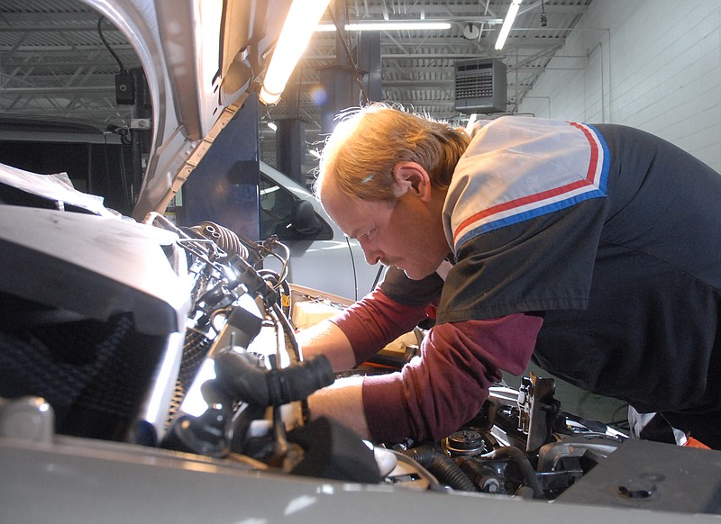 A mechanic at a local dealership works under the hood of a car.